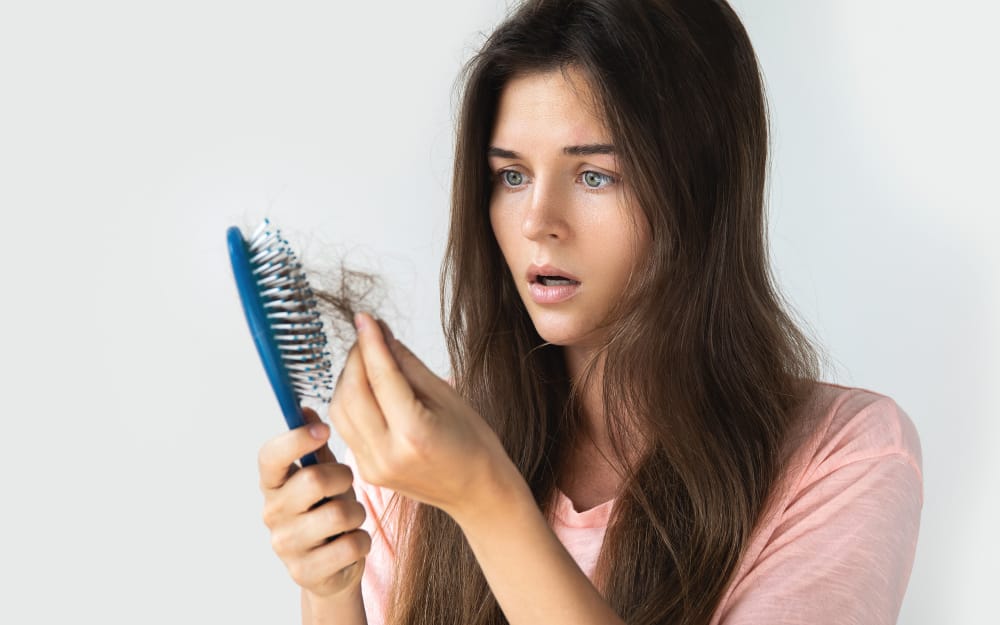 Woman looking at her scalp in concern, identifying early thinning suitable for hair rejuvenation