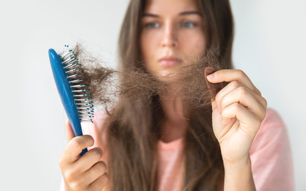Concerned woman inspecting her parting to evaluate hair loss before hair rejuvenation treatment